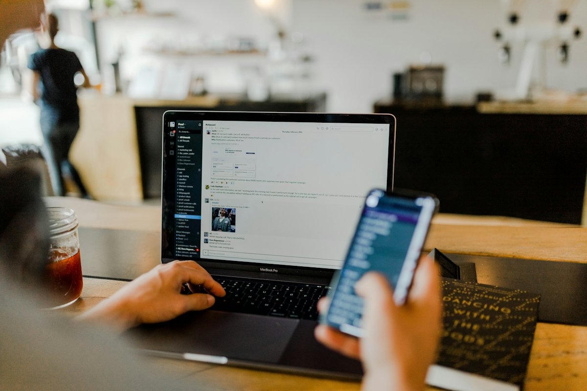 Person scrolling social media on a phone at a laptop